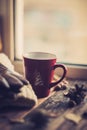 Hands in red knitted gloves holding a hot cup of coffee against yellow leaves background. Concept of autumn time, warmth and cozin Royalty Free Stock Photo