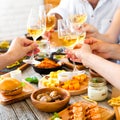 Hands with red wine toasting over served table with food.