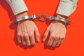 Hands restrained in handcuffs against bold red background, legal concept