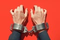 Hands restrained in handcuffs against bold red background, legal concept