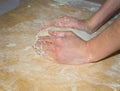 Hands rolls a ball of dough for pizza on homemade wooden Board with flour.