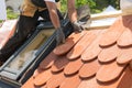 Hands of roofer laying tile on the roof. Installing natural red tile. Roof with mansard windows