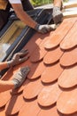 Hands of roofer laying tile on the roof. Installing natural red tile. Roof with mansard windows