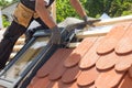Hands of roofer laying tile on the roof. Installing natural red tile using pliers. Roof with mansard windows