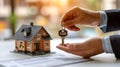 Hands of salesman holding key near house model and paper document on table. House selling or renting concept.