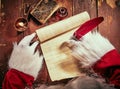 Hands of Santa Claus writing a Christmas letter on a vintage scroll with a red quill pen by candlelight on an old rustic wooden