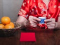 Hands of a senior woman wearing a traditional cheongsam qipao dress holding a teacup with red envelopes Ang Pao and four