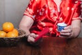 Hands of a senior woman wearing a traditional cheongsam qipao dress holding a teacup with red envelopes (Angpao)