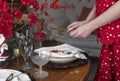 Hands setting festive dining table with plates, gold fork anf knife, red flowers for Christmas dinner, closeup Royalty Free Stock Photo