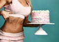 Hands of sexy pretty fitness slim woman in pink bra holding birthday cake with cream and pointing at slim sporty belly