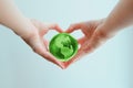 Hands in shape of heart holding green glass globe of South and North America