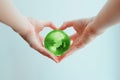 Hands in shape of heart holding green glass globe of South Pole