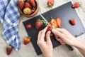 Hands slicing red ripe strawberries, with bowl and kitchen towel .