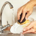 Hands with sponge wash the dirty dishes under running water in kitchen