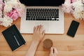 Hands on stylish laptop with coffee, phone with empty screen, black notebook and peonies on rustic wooden table. Freelance concept Royalty Free Stock Photo