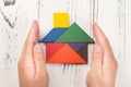 Hands surround a wooden house made by tangram home insurance concept and representing home ownership