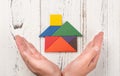 Hands surround a wooden house made by tangram home insurance concept or representing home owner ship