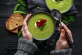 Hands in sweater, pullover holding cosy warming in cold weather. Sweet pea, leek and mint hot soup topped with crunchy bacon and d
