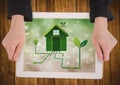 Hands with tablet on table showing green house graphic against bokeh Royalty Free Stock Photo