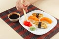 Hands taking ginger with chopsticks. Sushi with omelet with eel and with salmon and soy sauce on black and red bamboo mat. Royalty Free Stock Photo