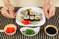 Hands taking ginger with chopsticks. Sushi set, hiyashi wakame salad, soy sauce and salmon caviar on black bamboo mat. Royalty Free Stock Photo