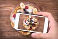 Hands taking photo pancakes with fresh fruit with smartphone.