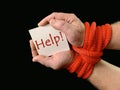 Hands tied with a rope, on a black background. Tied hands are holding a note with the inscription. Concept: loan, debt, help Royalty Free Stock Photo