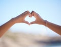 Hands together, heart sign and outdoor at beach, nature and blue sky in blurred background for love. Couple, hand touch