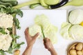 hands top view cutting cabbage on white chopping board on kitchen topwork with cauliflowers zucchini and potatoes