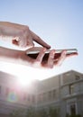 Hands touching phone against blurry building with flare Royalty Free Stock Photo