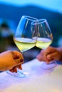 Hands with two clinking glasses of cold white wine in mountains cafe at night Royalty Free Stock Photo