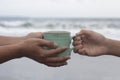 Hands of two people holding a cup of coffee or tea on beach background. Take and give or giving and receive concepts.