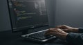 Hands typing on a black keyboard in front of a computer monitor displaying code with Royalty Free Stock Photo