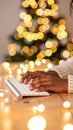 Hands typing on computer keyboard with warm bokeh Christmas tree lights in background Royalty Free Stock Photo