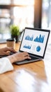 Hands typing on laptop displaying charts and graphs in a modern office setting with a coffee cup Royalty Free Stock Photo