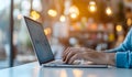 Hands typing on a laptop keyboard in a modern cafe setting with warm bokeh lights in the background creates a cozy work Royalty Free Stock Photo