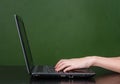 Hands typing on notebook near empty green chalkboard