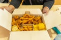 hands of an unrecognizable person opening a fast food box, with chicken, corn and french fries