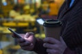 Hands using a phone texting on smartphone app and holding paper cup of coffee.