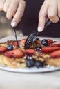 Hands using plastic silverware to cut blueberry and strawberry pancakes Royalty Free Stock Photo