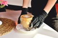 Hands of a waitress in medical gloves with a coffee mug, in a cafe