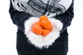 Hands in warm white mittens hold tangerines in winter