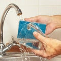 Hands wash the dirty glass under running water in kitchen