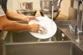 Hands washing dirty dishes with running water in kitchen sink