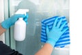 Hands wearing blue gloves holding a white plastic spray bottle and towel fabric cleaning home glass door for protect allergic Royalty Free Stock Photo