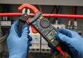 Hands wearing blue gloves are using a clamp meter to measure electrical current on a red cable. The Royalty Free Stock Photo