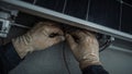 Closeup of hands connecting wires under a solar panel, technician wearing protective gloves Royalty Free Stock Photo