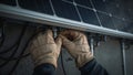 Closeup of hands connecting wires under a solar panel, technician wearing protective gloves Royalty Free Stock Photo