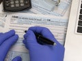 Hands Wearing Rubber Gloves Filling Out an IRS 1040 tax form in 2020