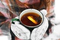 Hands in white mittens, holds a green mug of tea, and snow in winter Royalty Free Stock Photo